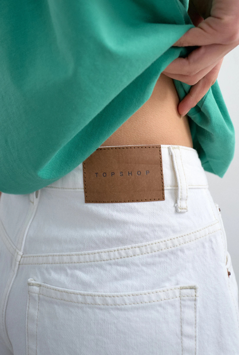 Back detail image of a model wearing Vigga high rise white denim shorts in white, by brand Top shop